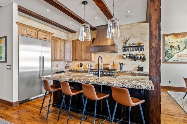 kitchen with wood finished floors, premium range hood, built in fridge, and baseboards