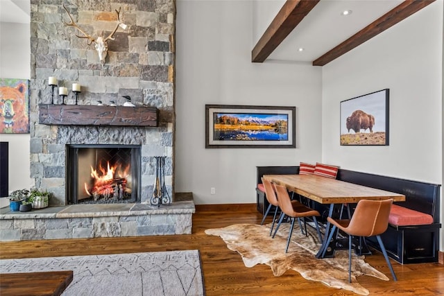 dining area with recessed lighting, a stone fireplace, wood finished floors, beamed ceiling, and baseboards