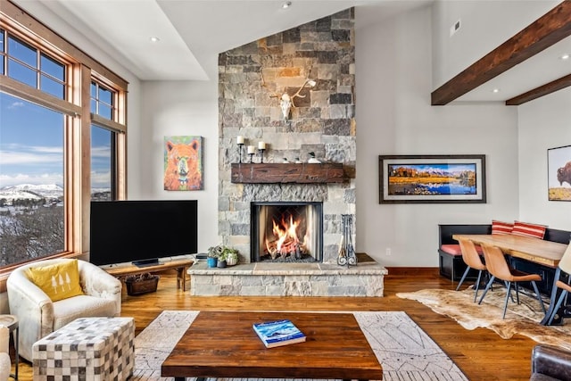 living room with recessed lighting, lofted ceiling with beams, a stone fireplace, wood finished floors, and baseboards