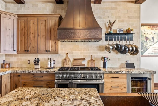 kitchen featuring tasteful backsplash, brown cabinetry, range with two ovens, light stone counters, and custom exhaust hood