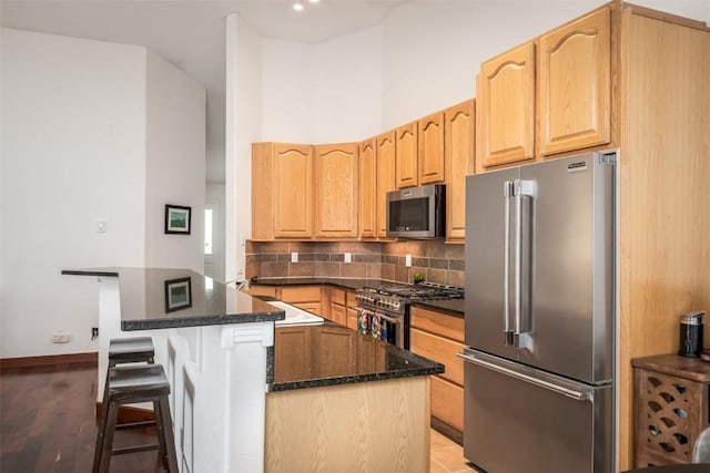 kitchen with high end appliances, a breakfast bar, light brown cabinetry, and backsplash
