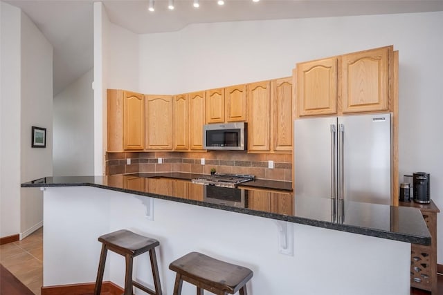 kitchen featuring stainless steel appliances, dark stone countertops, light brown cabinetry, and backsplash