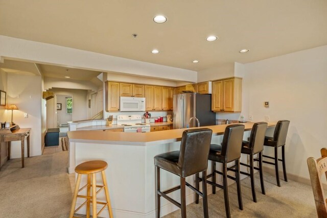 1724 Ski Time Square Dr Unit R5, Steamboat Springs, CO 80487 - kitchen with white appliances, a peninsula, light colored carpet, recessed lighting, and a breakfast bar area