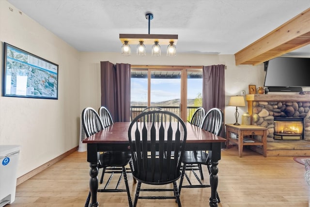 dining room with baseboards, light wood finished floors, and a stone fireplace