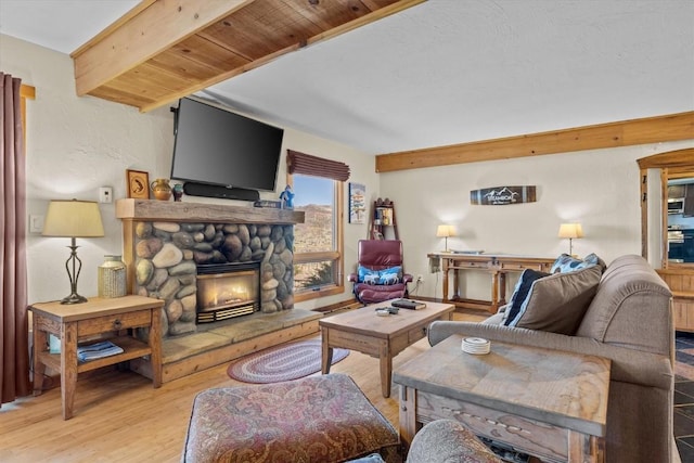 living room with a stone fireplace, wood finished floors, and beam ceiling