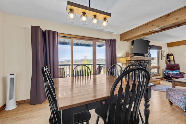 dining area featuring a stone fireplace, light wood-type flooring, beam ceiling, and a wealth of natural light