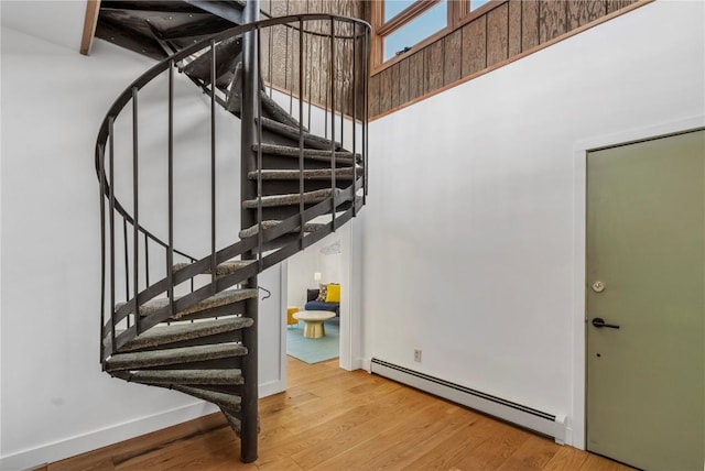 staircase with baseboards, wood finished floors, a towering ceiling, and a baseboard radiator