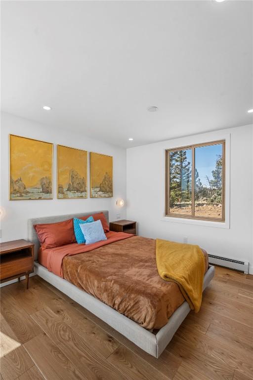 bedroom with a baseboard heating unit, wood finished floors, and recessed lighting