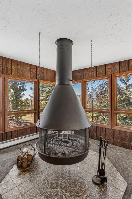 details with wooden walls, a wood stove, carpet floors, a textured ceiling, and baseboard heating