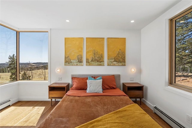 bedroom with a baseboard heating unit, wood finished floors, and multiple windows