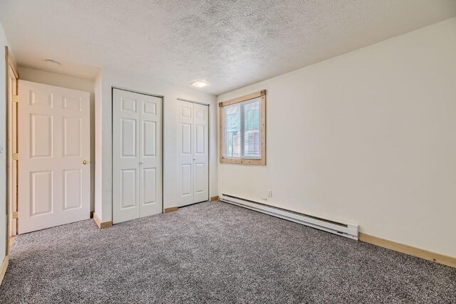 unfurnished bedroom with a baseboard heating unit, a textured ceiling, baseboards, multiple closets, and carpet floors