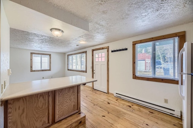 kitchen featuring a peninsula, a textured ceiling, freestanding refrigerator, light wood-style floors, and a baseboard radiator