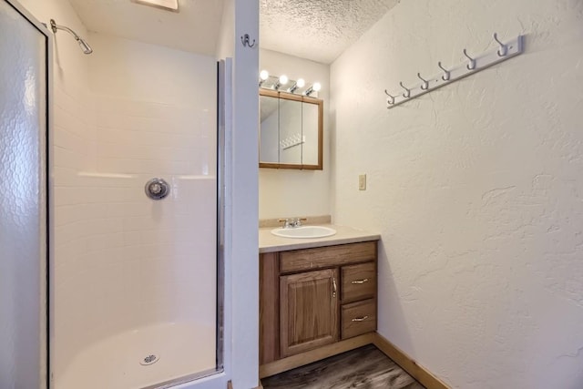 full bathroom with a textured ceiling, wood finished floors, a shower stall, a textured wall, and vanity