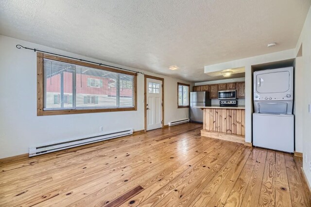 unfurnished living room with a baseboard radiator, light wood finished floors, stacked washing maching and dryer, and a textured ceiling