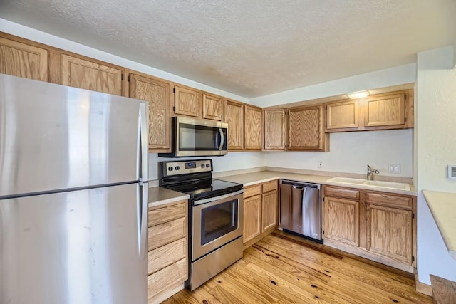 kitchen featuring a textured ceiling, a sink, light wood-type flooring, stainless steel appliances, and light countertops