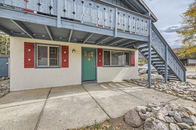 view of front of home with stucco siding, stairway, and a patio