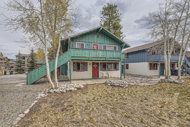 view of front of property featuring board and batten siding, a wooden deck, stairs, and a patio
