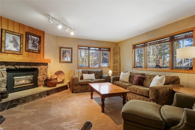 carpeted living area with track lighting, a stone fireplace, and a wealth of natural light
