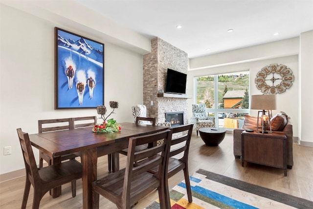 dining area with light wood-type flooring, recessed lighting, baseboards, and a stone fireplace