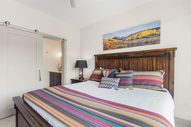 bedroom with a barn door, carpet, ceiling fan, and ensuite bath