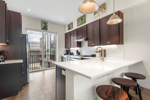 kitchen with a breakfast bar area, light wood-style flooring, freestanding refrigerator, a peninsula, and decorative backsplash