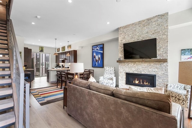 living area with stairs, recessed lighting, a stone fireplace, and light wood finished floors