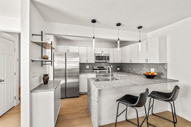 kitchen featuring appliances with stainless steel finishes, white cabinets, a sink, and a peninsula