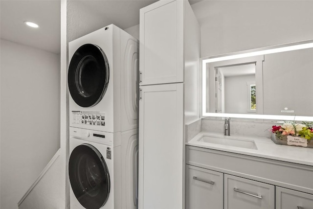 washroom featuring cabinet space, a sink, stacked washer and clothes dryer, and recessed lighting