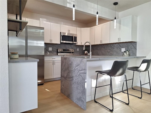 kitchen with stainless steel appliances, white cabinetry, a kitchen breakfast bar, light wood-type flooring, and decorative light fixtures