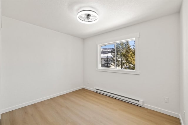 unfurnished room with baseboard heating, light wood-style flooring, and baseboards