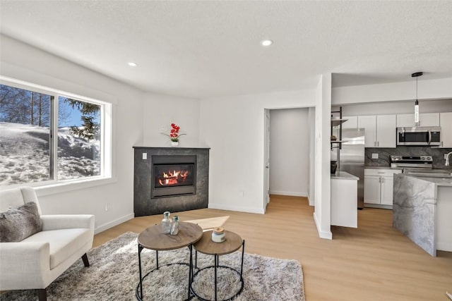 living room featuring light wood finished floors, recessed lighting, baseboards, and a glass covered fireplace