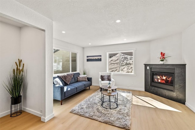 living room featuring recessed lighting, a glass covered fireplace, a textured ceiling, wood finished floors, and baseboards