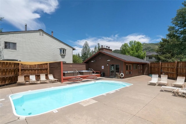 community pool featuring fence, a hot tub, a wooden deck, and a patio