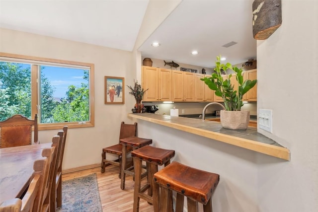 1508 Cascades Dr Unit 4, Steamboat Springs, CO 80487 - kitchen featuring light brown cabinets, a breakfast bar area, light wood-type flooring, recessed lighting, and vaulted ceiling