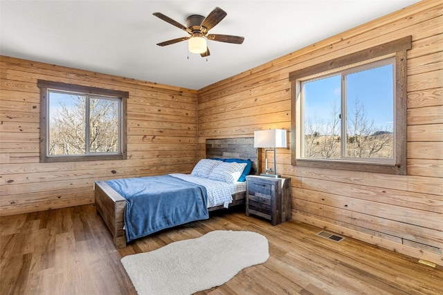 bedroom featuring wood finished floors, visible vents, wood walls, and ceiling fan