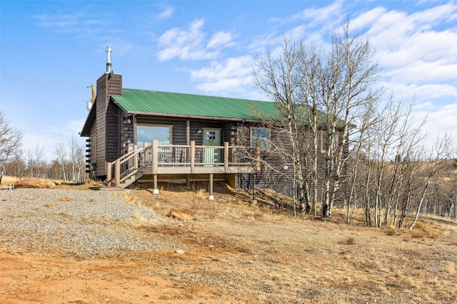 view of front facade featuring a chimney, log exterior, a deck, and metal roof