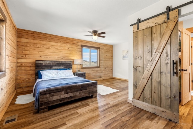 bedroom with a barn door, wood finished floors, baseboards, wood walls, and visible vents