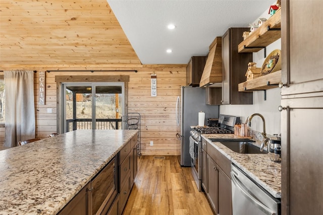 kitchen featuring open shelves, a sink, wooden walls, premium range hood, and appliances with stainless steel finishes