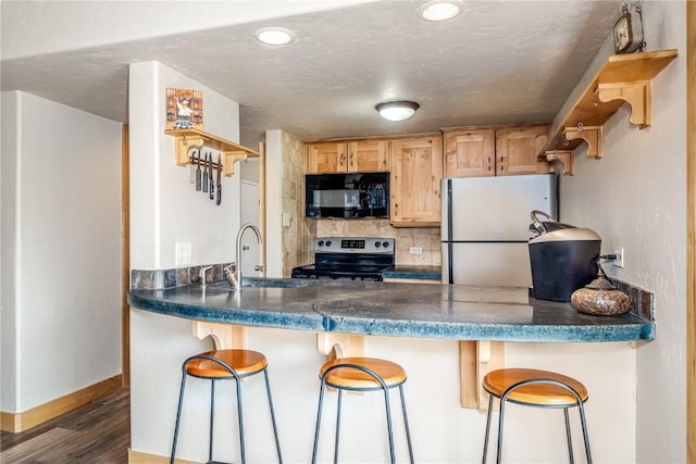 kitchen featuring dark countertops, wood finished floors, black microwave, stainless steel electric stove, and freestanding refrigerator