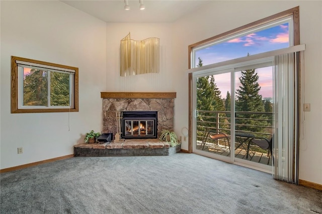 unfurnished living room with carpet floors, a stone fireplace, and baseboards