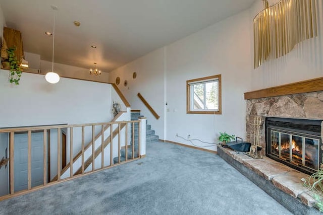 carpeted living room featuring an inviting chandelier, stairs, a stone fireplace, and baseboards