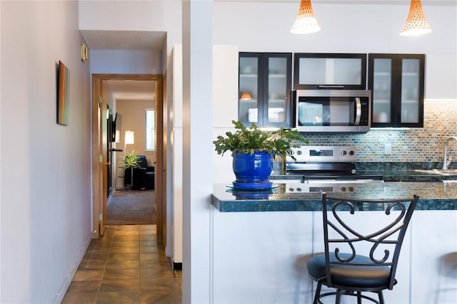 72 Corinthian Cir Unit 303, Dillon, CO 80435 - kitchen featuring appliances with stainless steel finishes, backsplash, a kitchen bar, glass insert cabinets, and dark countertops