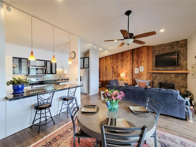 72 Corinthian Cir Unit 303, Dillon, CO 80435 - dining room featuring wood walls, rail lighting, wood finished floors, a ceiling fan, and a stone fireplace