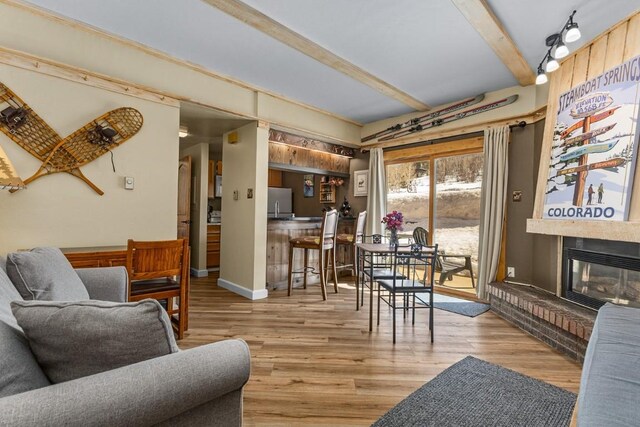 living room with beamed ceiling, a glass covered fireplace, and wood finished floors