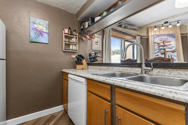kitchen with brown cabinets, wood finished floors, a sink, white dishwasher, and baseboards