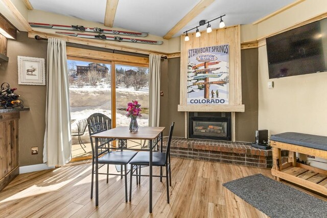dining room featuring baseboards, wood finished floors, a large fireplace, and beamed ceiling