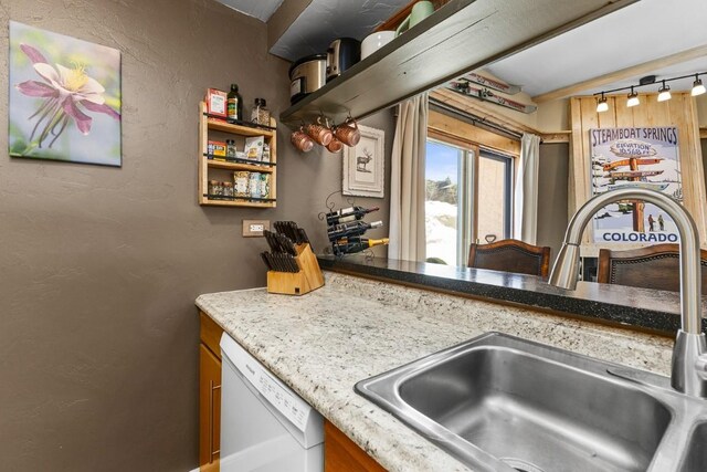 kitchen with a sink, dishwasher, a textured wall, rail lighting, and light stone countertops