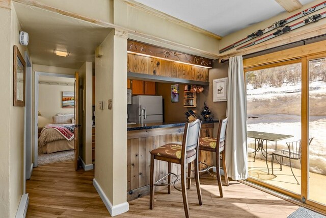 kitchen featuring light wood finished floors, dark countertops, freestanding refrigerator, and a breakfast bar area