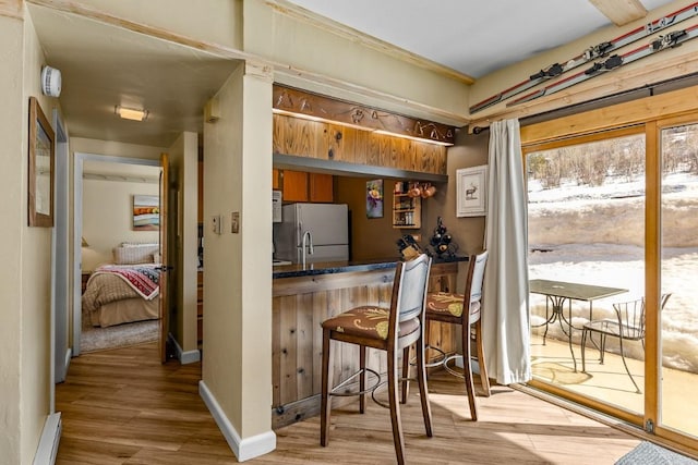 1945 Cornice Rd Unit 101D, Steamboat Springs, CO 80487 - kitchen with freestanding refrigerator, light wood-style floors, dark countertops, a breakfast bar area, and brown cabinets