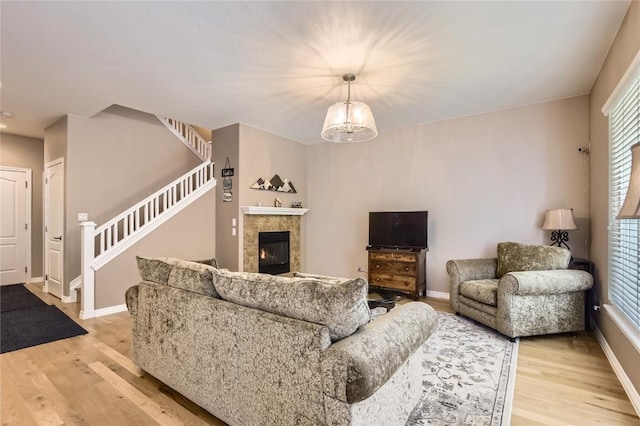 living area featuring light wood-type flooring, baseboards, stairway, and a tiled fireplace